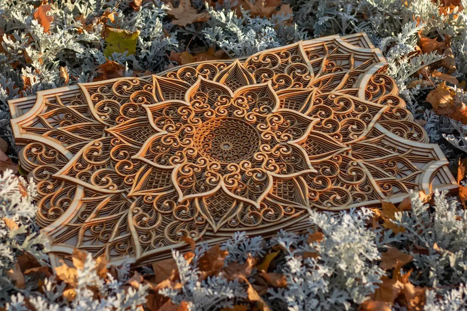 A wooden mandala with intricate geometric patterns, 3D laser-cut, displayed on a bed of autumn leaves.