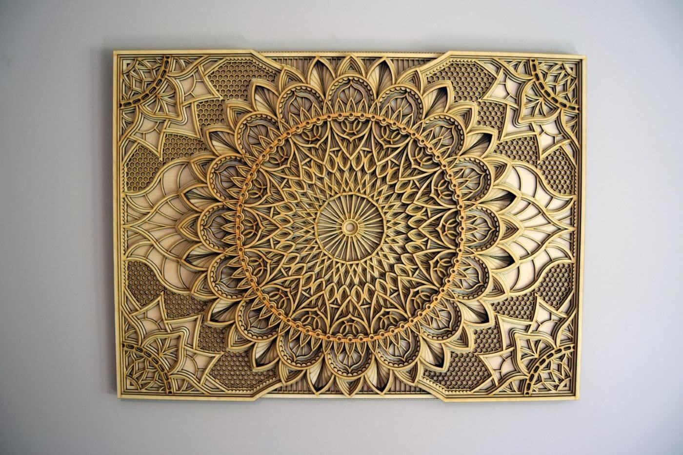 A wooden mandala with intricate geometric patterns and a central sun design, with a beige and brown color palette.